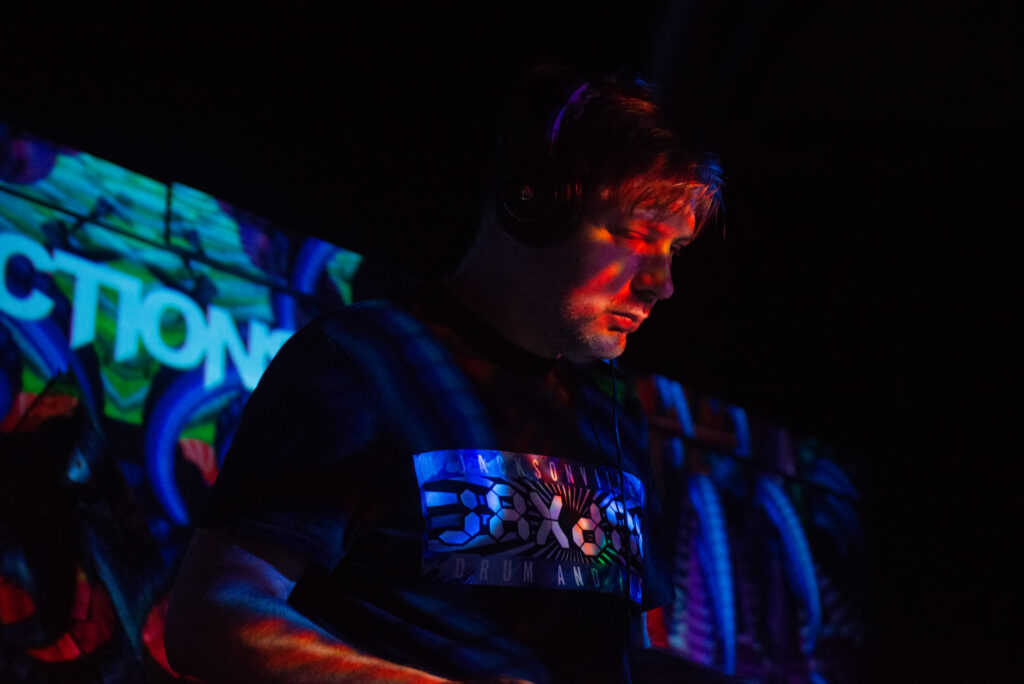 Reflections wearing a JaxDnB shirt in a dimly lit venue