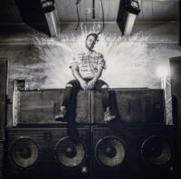 bass artist Sub-Lo sitting atop a stack of speakers